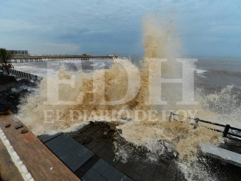 inmensidad del Océano Pacífico, con olas grandes y amenazantes rompiendo cerca del histórico muelle de pescadores del Puerto de La Libertad, el cual aparece vacío.