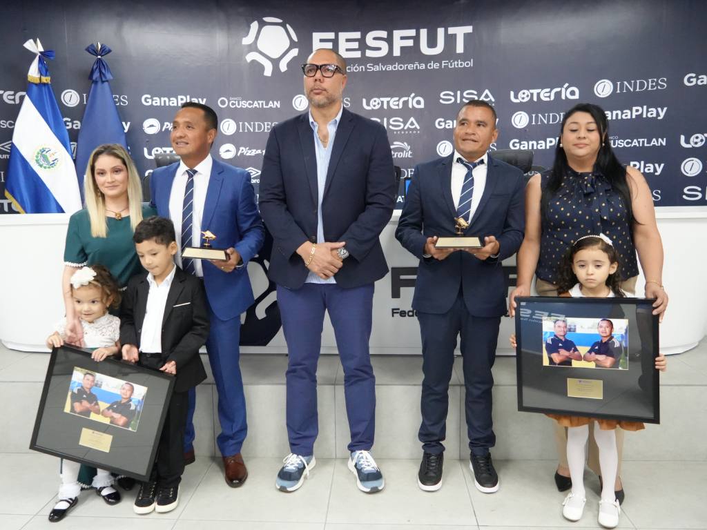 Fotografía familiar y grupal al cierre de la ceremonia. Posan en el centro los homenajeados e invitados principales junto a sus familiares (esposas e hijos), quienes también sostienen los cuadros conmemorativos y placas, celebrando juntos el reconocimiento otorgado por la federación.