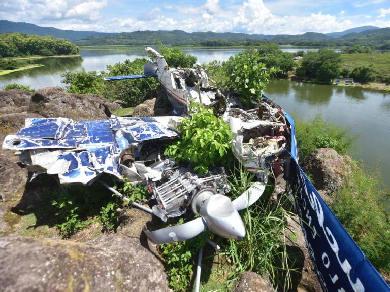 Una toma en ángulo picado que revela la magnitud del impacto: el motor de la avioneta y su hélice doblada descansan entre la maleza en primer plano, seguidos por las alas destrozadas y el fuselaje que se proyecta hacia el lago Suchitlán.