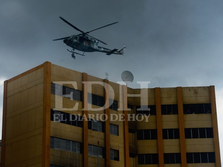 Un helicóptero militar de rescate vuela a baja altura directamente sobre la azotea del edificio del Ministerio de Hacienda bajo un cielo gris. Del helicóptero cuelga una cuerda de rescate con una persona suspendida en el aire mientras se realizan las labores de evacuación de los sobrevivientes en la parte alta de la estructura.
