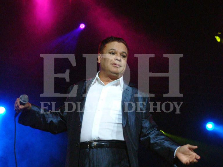 Juan Gabriel saludando alegremente en el escenario rodeado por integrantes de su mariachi.