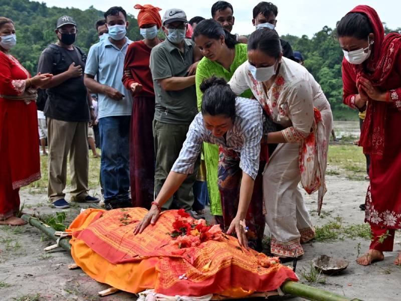 Una mujer desconsolada llora frente a la pira funeraria de su hijo durante una ceremonia de cremación al aire libre en Nepal.