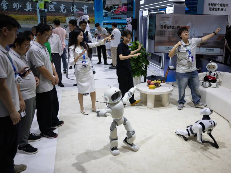 Grupo de personas bailando codo a codo con robots interactivos durante un evento tecnológico de robótica.