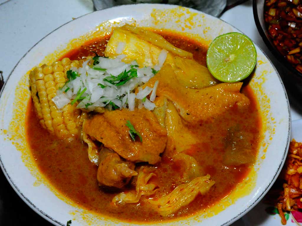 Plato servido de sopa de pata con elote, verdura, mondongo y toque de cilantro.