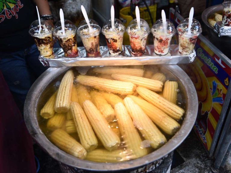 Olla con elotes sancochados listos para prepararse con salsa negra, queso, mayonesa y salsa de tomate al gusto de la feria.