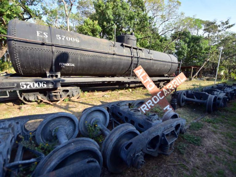 Viejos ejes de ferrocarril reposan oxidados en el suelo junto a un tanque cisterna en Sonsonate.