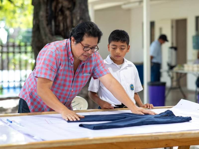 Estudiantes en un salón de clases recibiendo la medición de tallas de calzado y uniformes por parte del personal.