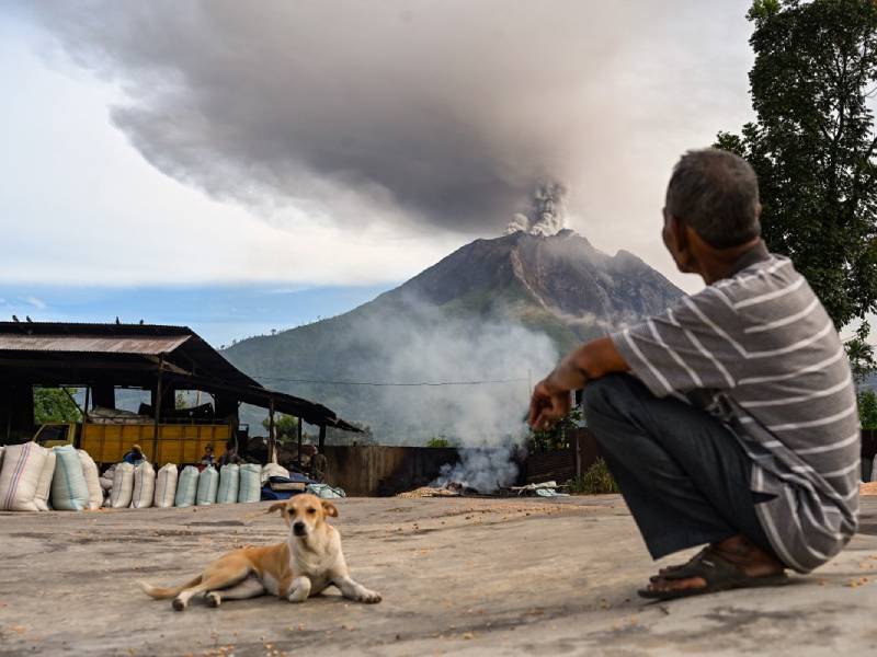 Hombre observando a lo lejos la erupción del volcán Sinabung, el cual expulsa una gran nube de ceniza y humo al amanecer.