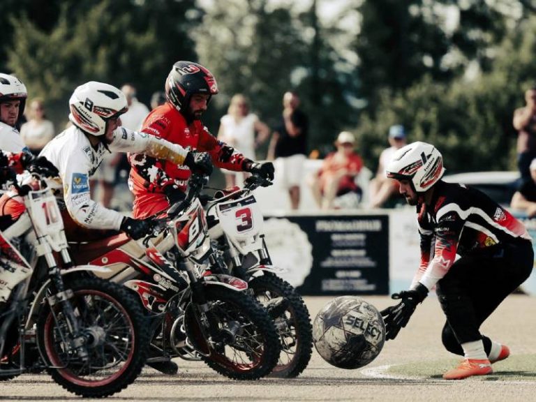Jugadores en motocicletas compiten por un balón gigante en una cancha de motoball.