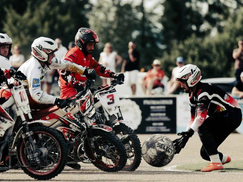 Jugadores en motocicletas compiten por un balón gigante en una cancha de motoball.