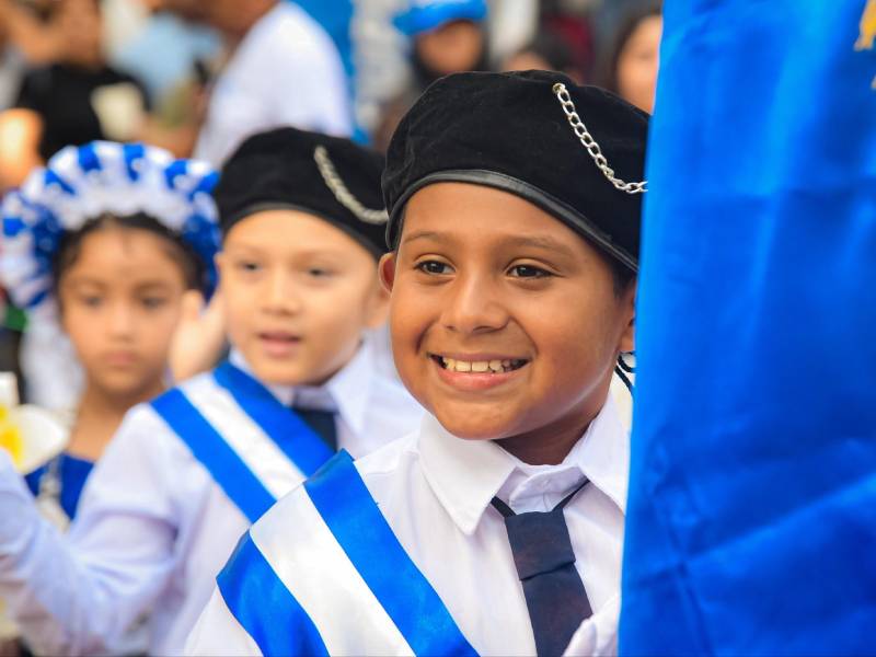La ministra de Educación declara ante la prensa acompañada por docentes y niños participantes en el desfile cívico.
