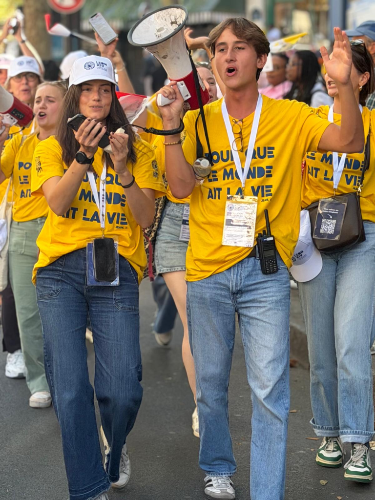 Jóvenes voluntarios animando con megáfonos en las calles durante la visita del Papa León a París Francia.