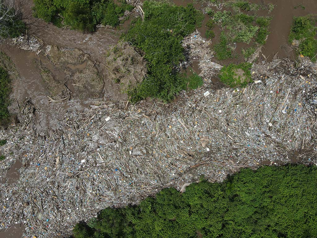 Toma cenital de alta resolución mostrando la densidad de plásticos, ramas y basura atascada en el río.