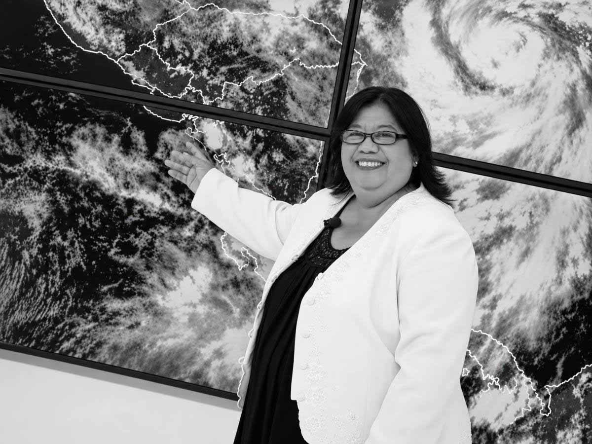 Sandra Yanira Martínez sonriendo y señalando una pantalla gigante con mapas satelitales en blanco y negro.