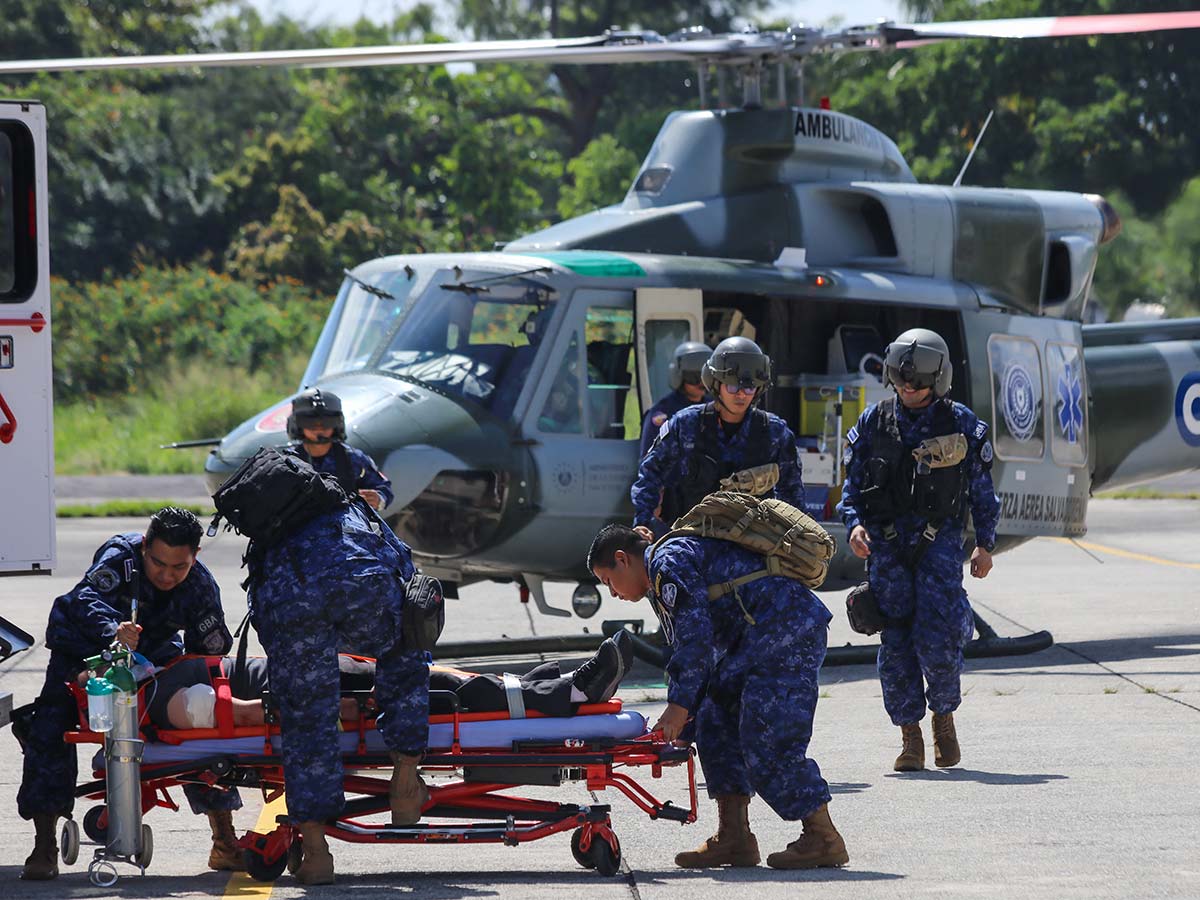 Equipo de rescate militar salvadoreño asistiendo a una persona herida en camilla tras descender de un helicóptero ambulancia.